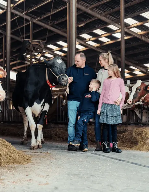 Familie Bornholdt mit einer schwarzbunten Kuh im Stallgang