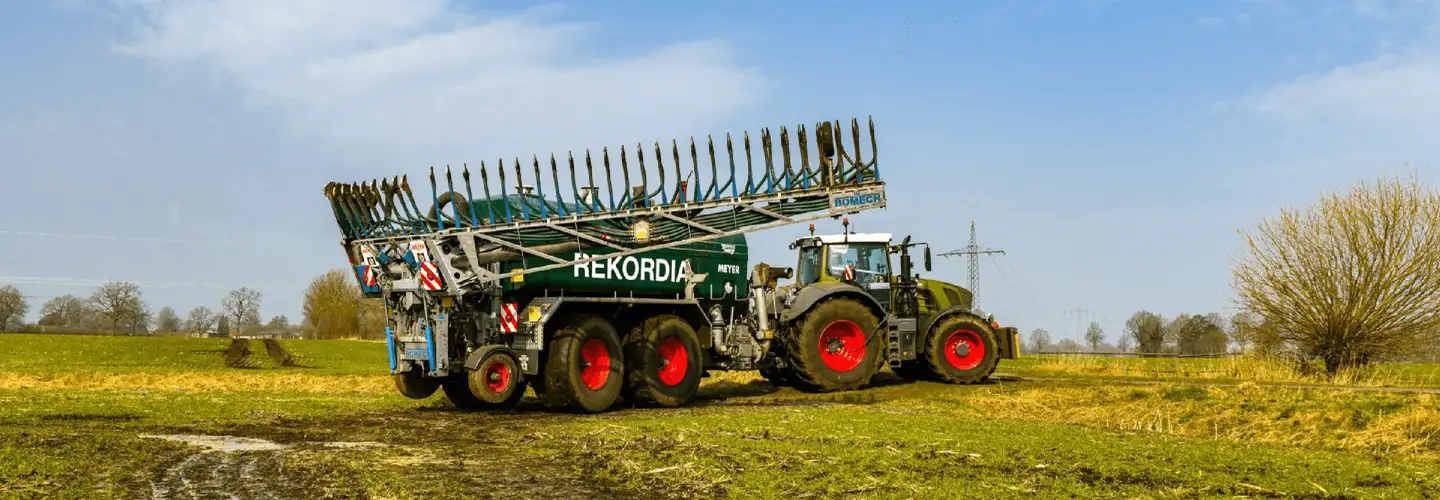 Grüner Traktor mit Güllefass und ausgeklapptem Schleppschlauch-Verteiler auf dem Feld
